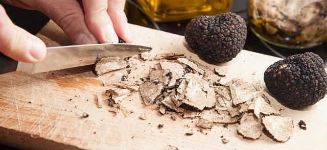 Découpe au couteau de truffe sur une planche en bois, lamelles et deux belles truffes